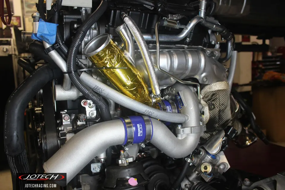 Close-up of a performance engine bay featuring turbo boost piping, HKS clamps, and gold heat reflective wrap.