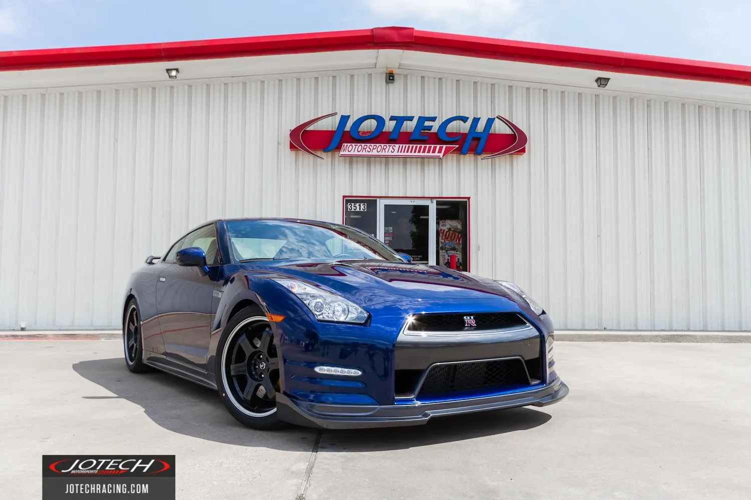 Blue Nissan GT-R parked outside Jotech Motorsports performance tuning shop with aftermarket wheels and front splitter.