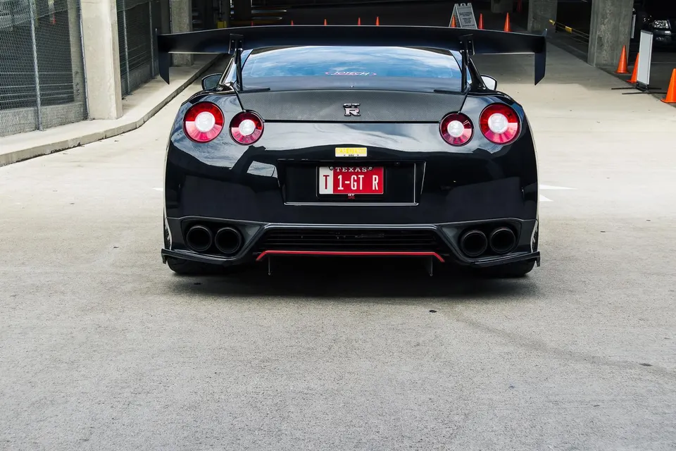 Rear view of a black Nissan GT-R with a large aftermarket carbon fiber wing, quad exhaust tips, and a red diffuser.