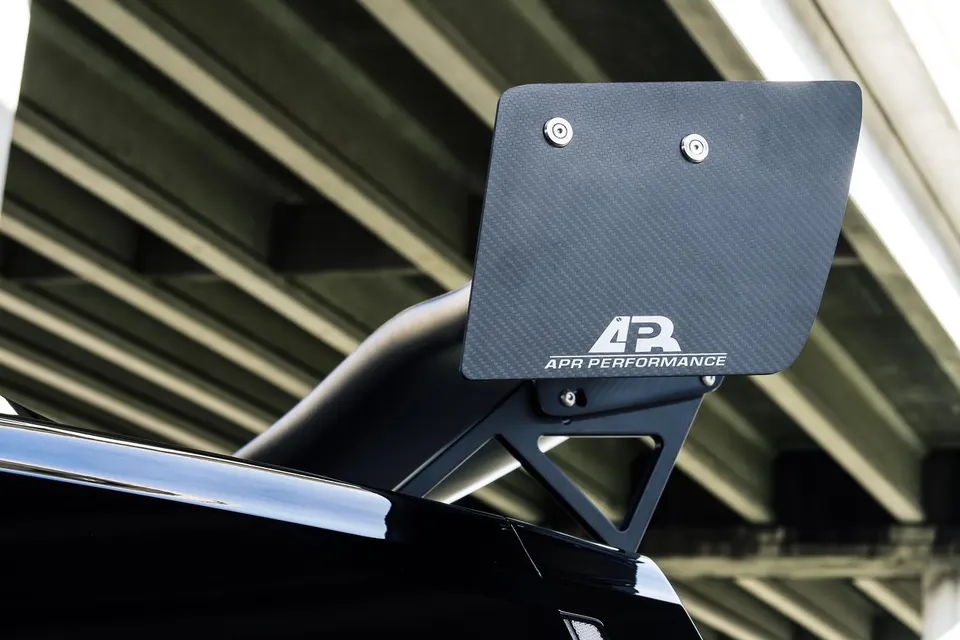 Close-up of an APR Performance carbon fiber rear wing on a car, showcasing its aerodynamic design.