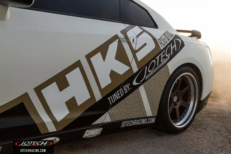 Side view of a white Nissan R35 GT-R with HKS and Jotech Motorsports livery and aftermarket wheels.