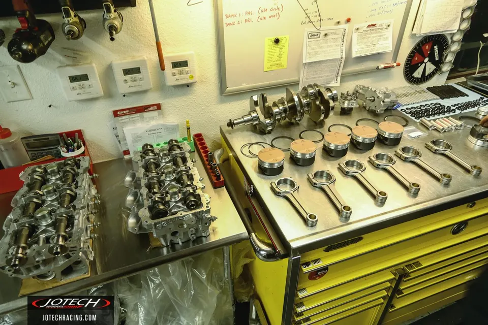 Engine internals laid out on a workbench in a performance tuning shop, including crankshaft, pistons, and connecting rods.