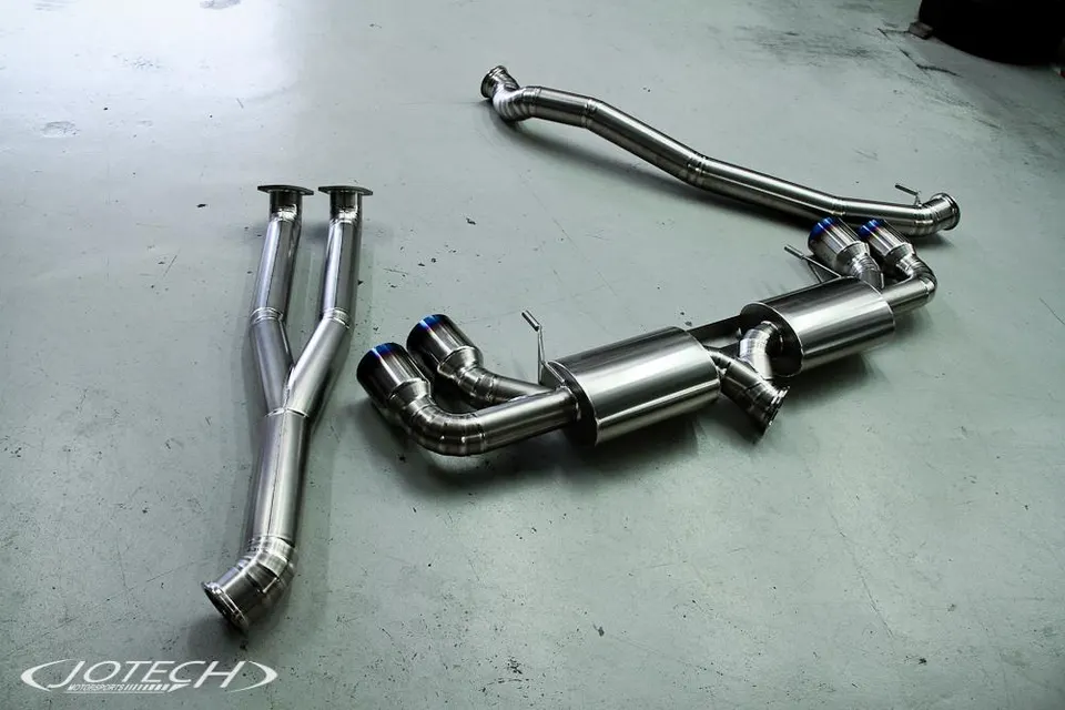 New titanium exhaust system components including mid-pipe, muffler, and blue-tipped exhaust tips laid out on a shop floor.
