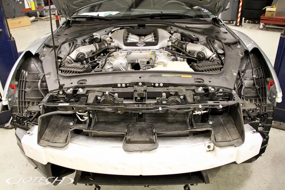 Nissan GT-R with front bumper removed, exposing the engine bay, intercooler, and front end components during shop work.