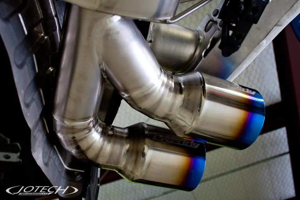 Close-up of a GReddy exhaust system with burnt titanium tips installed on a performance car.