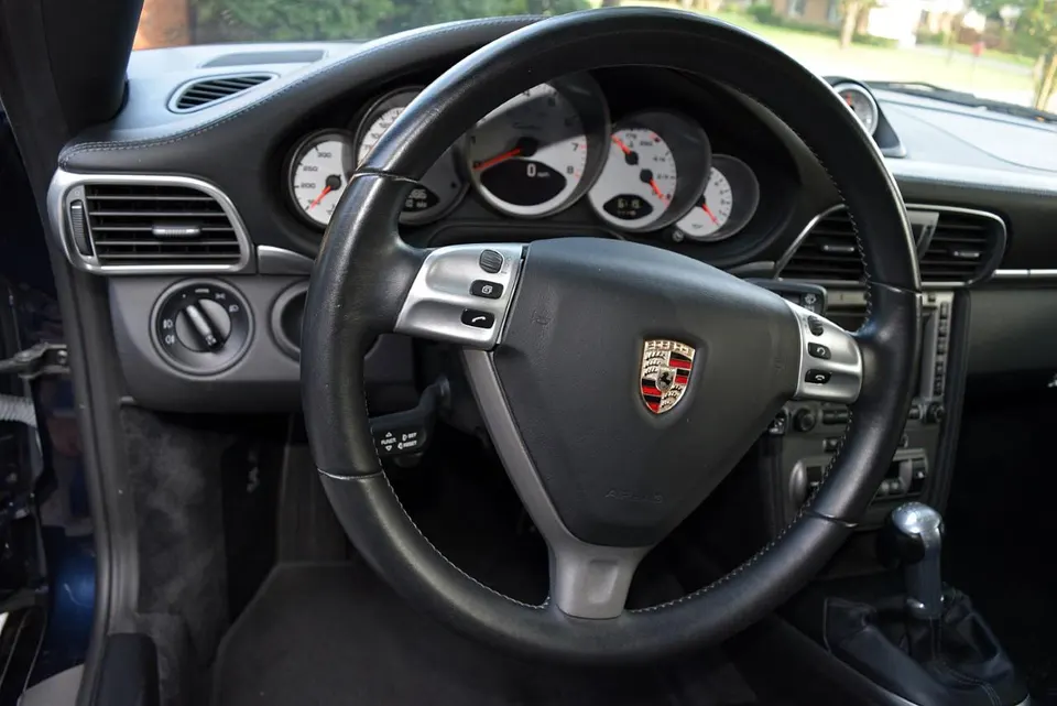 Interior view of a Porsche with a black leather steering wheel, dashboard, and gauges.
