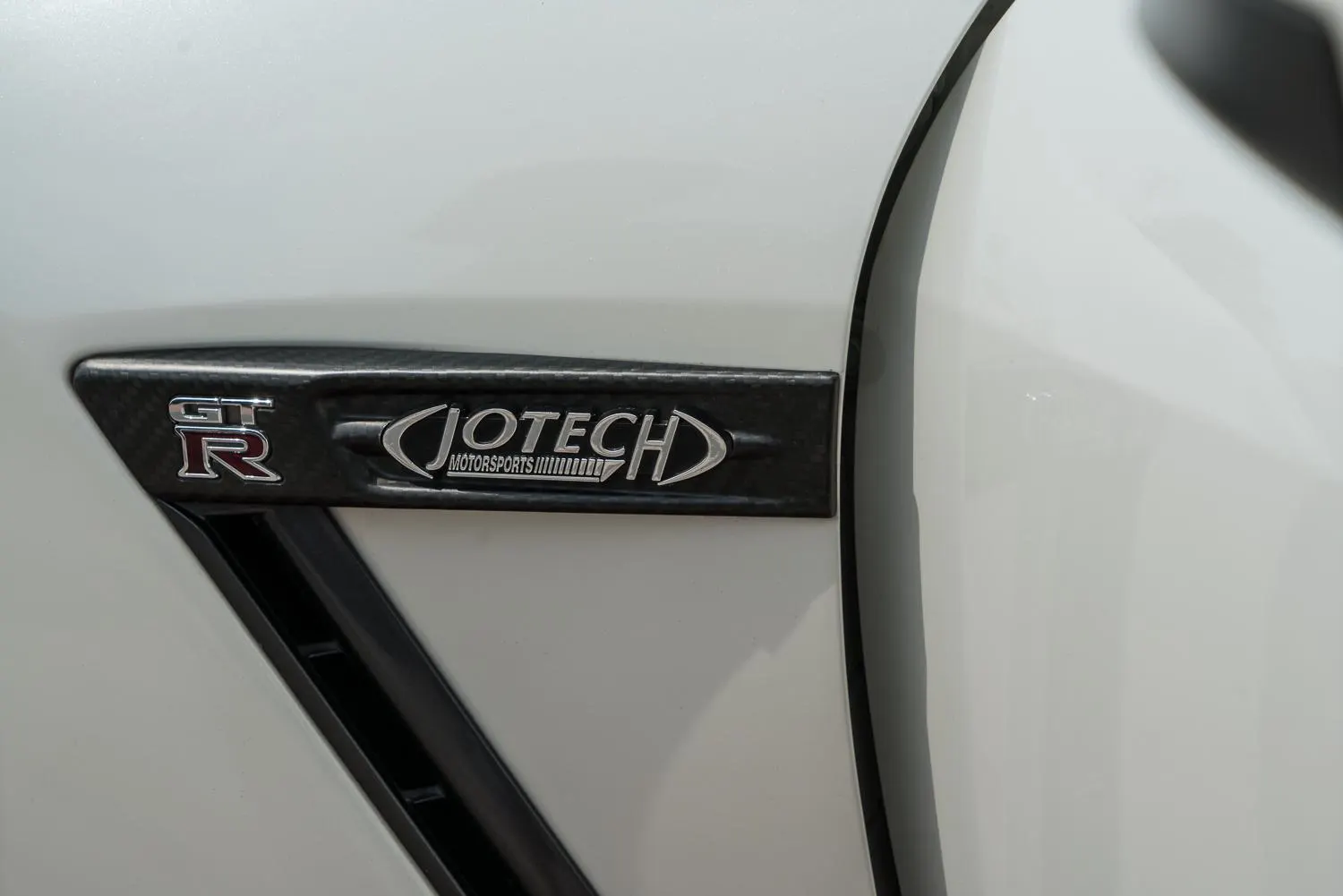 Close-up of a white Nissan GT-R's side vent with a carbon fiber trim and Jotech Motorsports badge.
