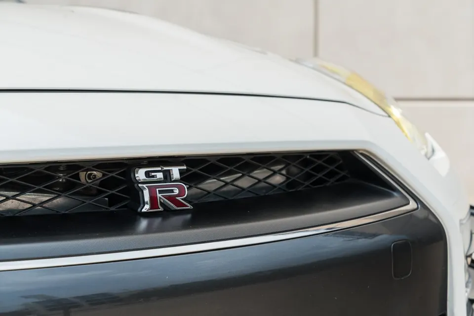Close-up of a white Nissan GT-R's front grille featuring the iconic GT-R badge.