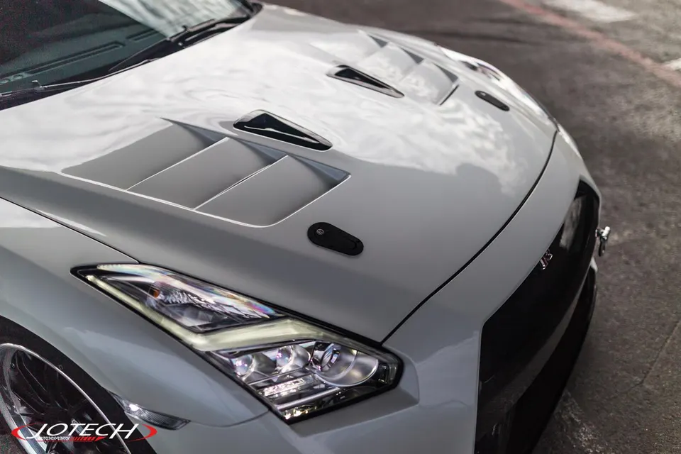 Close-up of a white Nissan GT-R's front end, showcasing a vented hood, hood pins, and LED headlights.