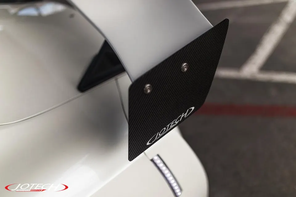 A close-up of a white car's carbon fiber rear wing with Jotech branding.