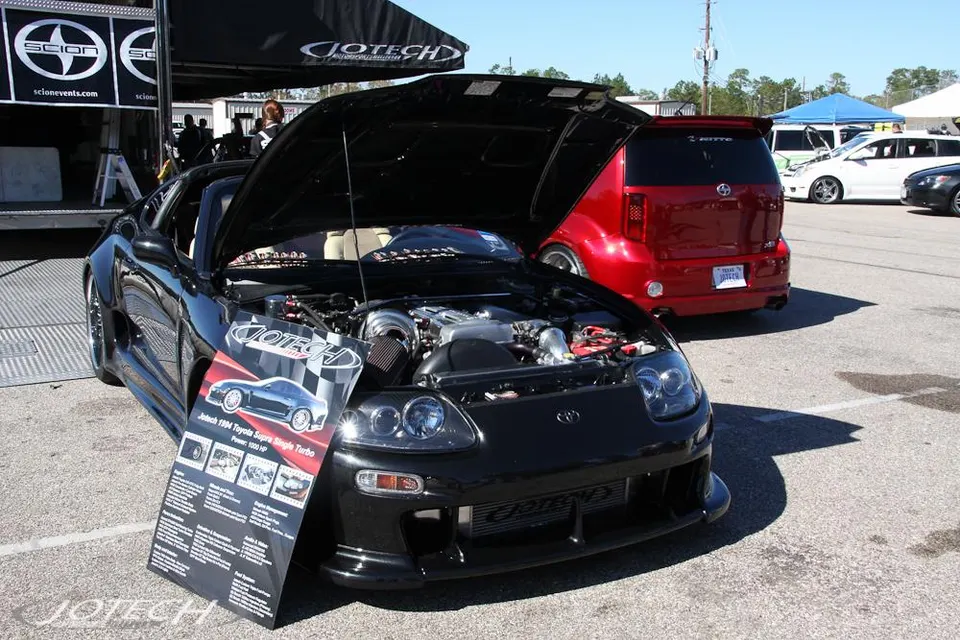 Black Jotech 1994 Toyota Supra single turbo with hood open displaying the engine bay at an outdoor car show.