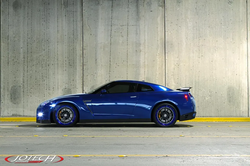 Blue Nissan GT-R with custom aftermarket wheels parked in a concrete tunnel, showcasing its side profile.