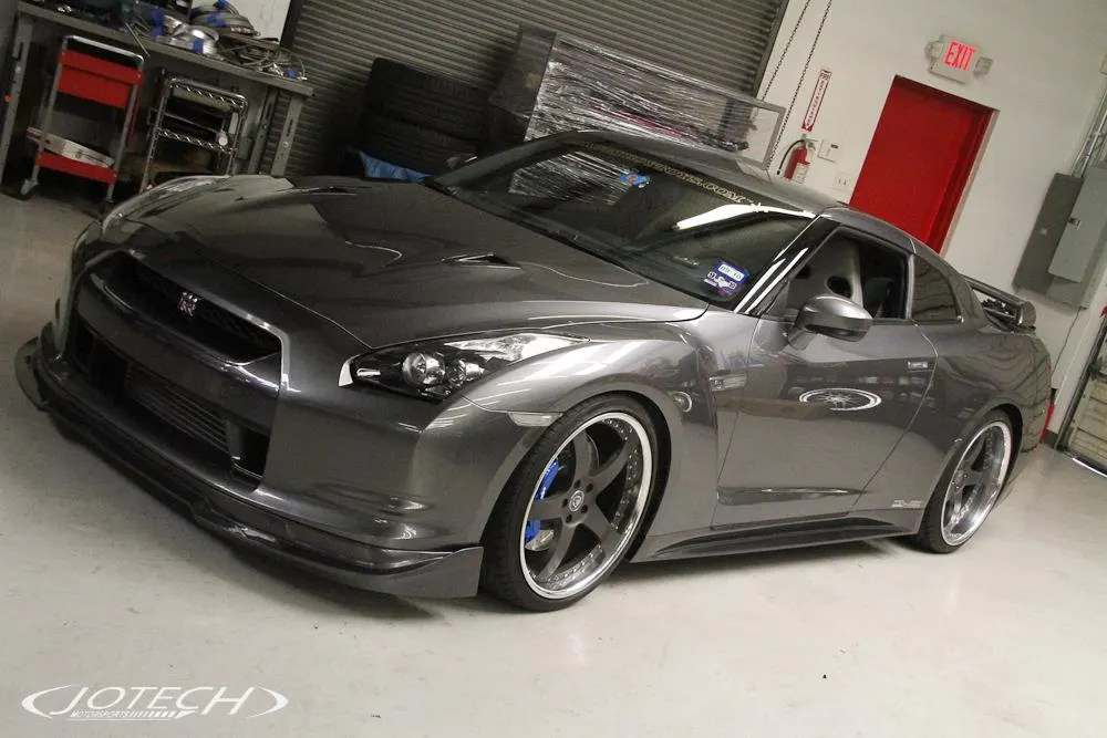 A grey Nissan GT-R with aftermarket wheels and an aero kit parked inside a Jotech Motorsports shop.