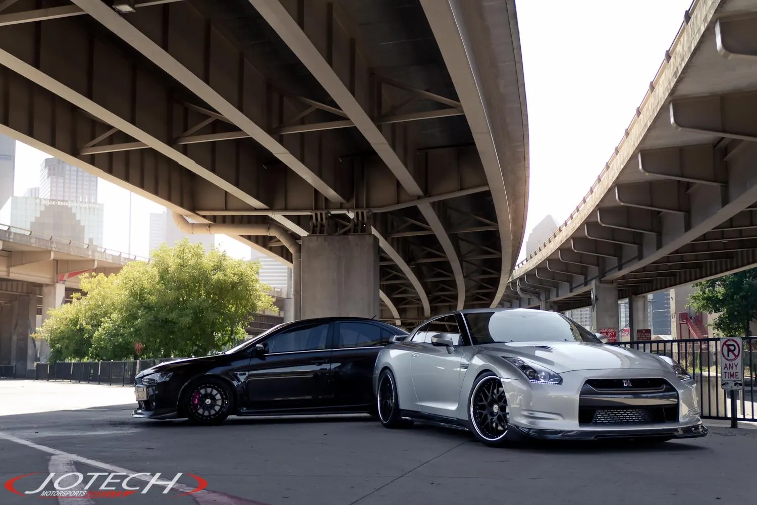 A black Mitsubishi Lancer Evolution X and a silver Nissan GT-R R35 parked under an urban overpass.
