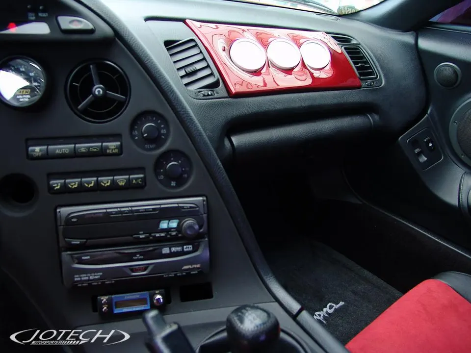 Interior view of a Toyota Supra dashboard with aftermarket gauges, Alpine radio, and red trim.