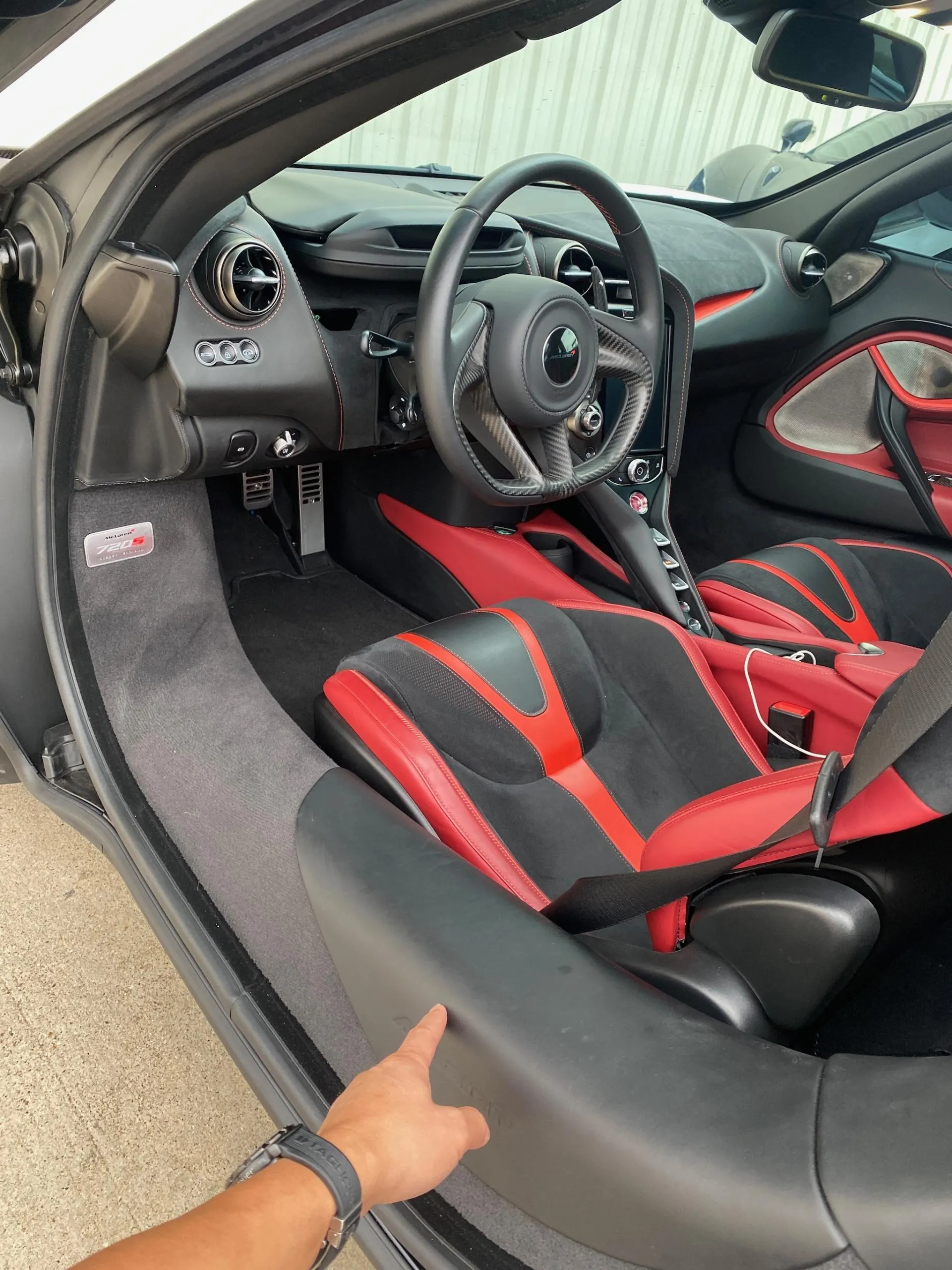 Interior view of a McLaren 720S with black and red seats, carbon fiber steering wheel, and dashboard.
