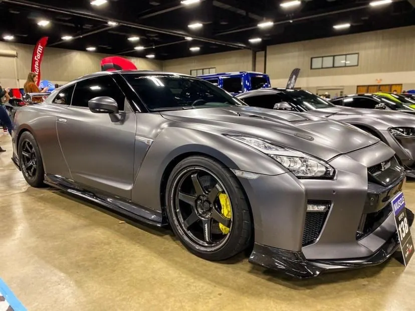 Matte grey Nissan GT-R with aftermarket wheels and carbon fiber aero kit displayed at a car show.
