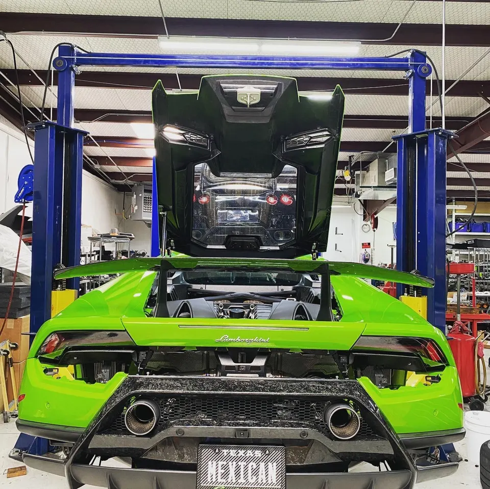 Green Lamborghini Huracan on a lift in a performance tuning shop with the engine bay open and rear bumper removed.