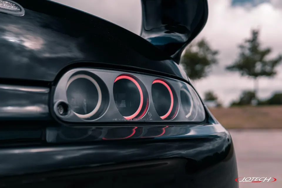 Close-up of a black Toyota Supra MK4's iconic round LED taillights and rear wing.