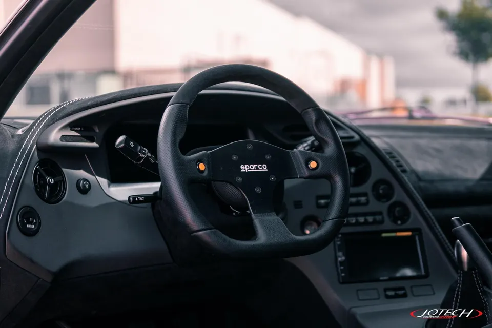 Close-up of a custom Sparco steering wheel and dashboard in a performance car, likely a Toyota Supra.