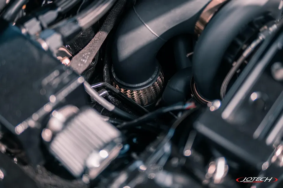 Close-up view of a high-performance engine bay featuring black boost piping and a braided line, likely part of a turbo system.