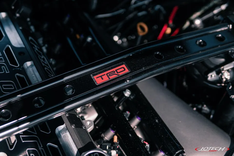 Close-up of a TRD strut bar installed in a performance car's engine bay, featuring custom components.