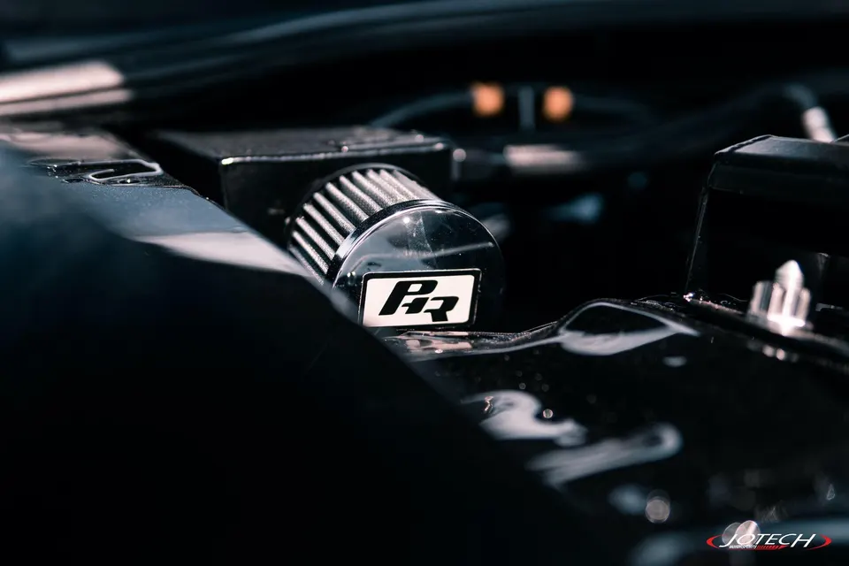 Close-up of a performance air filter with a PR logo in a dark engine bay, highlighting the induction system.