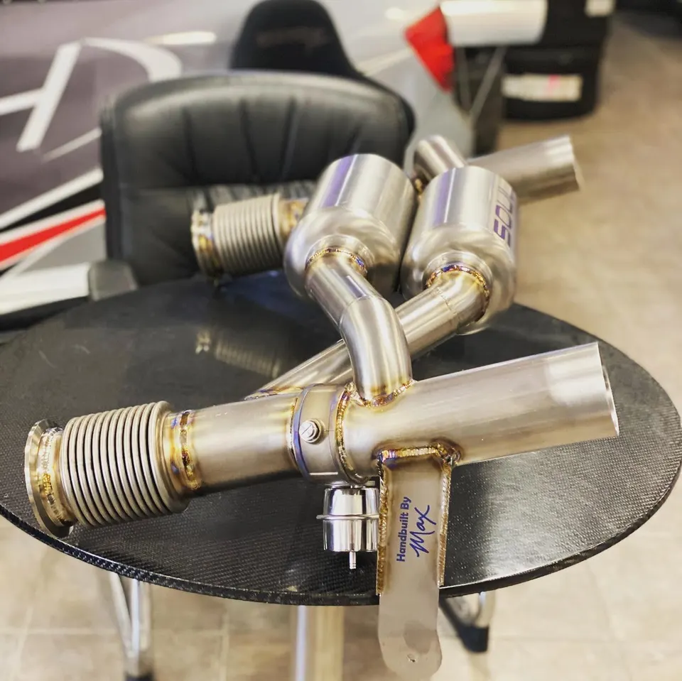 Titanium aftermarket exhaust system with visible welds and mufflers on a carbon fiber table, ready for installation.