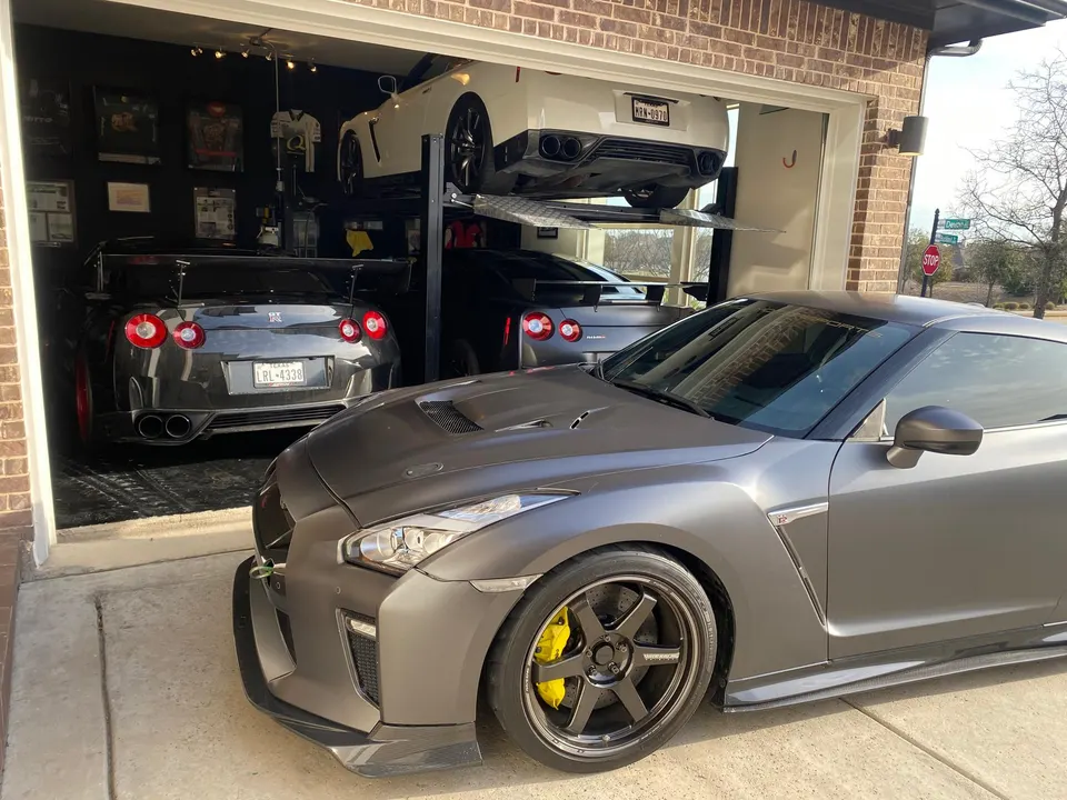 Multiple Nissan GT-Rs, including a grey one with aftermarket wheels and yellow calipers, parked in a garage with a car lift.