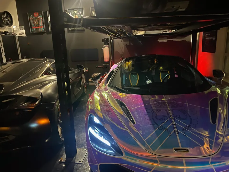 Two exotic cars, a custom-wrapped McLaren and a dark hypercar, parked in a well-lit garage.