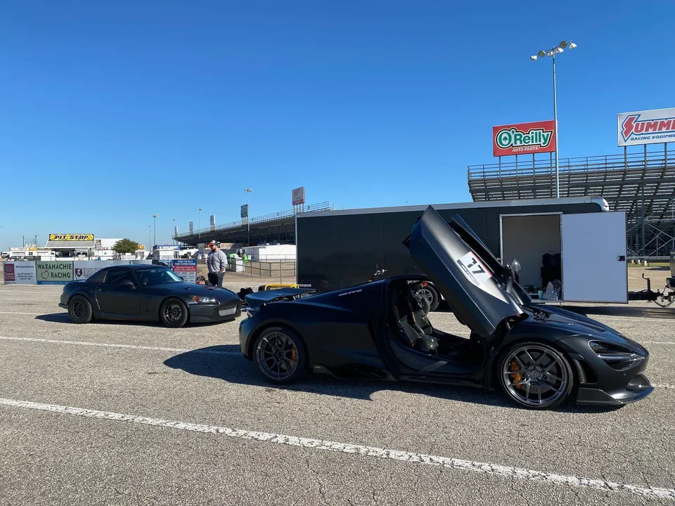 Honda S2000 and McLaren 720S parked in the paddock area of a racetrack on a sunny day.