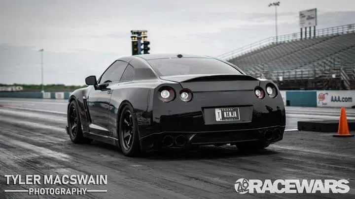 Black Nissan GT-R with a custom 'T NINJA' license plate on a drag strip, seen from the rear.