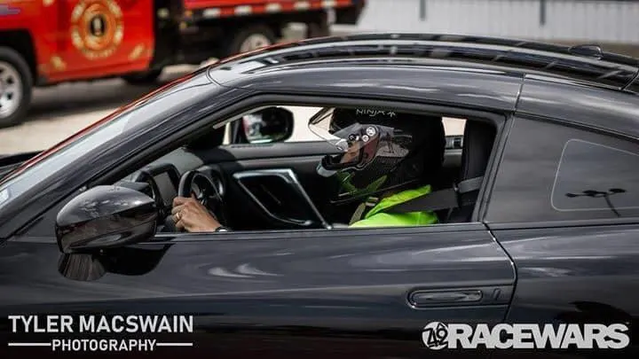 Black Nissan GT-R with a driver in a helmet on a track during a Racewars event.