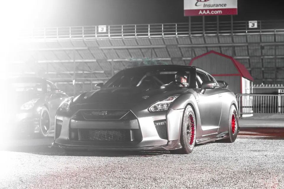 Silver Nissan GT-R with red wheels in the staging lane at a drag strip, ready for a race.