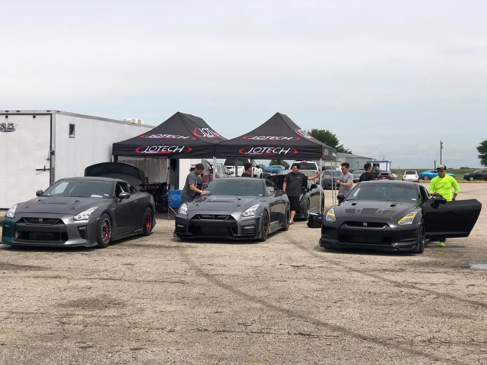 Multiple modified Nissan GT-Rs parked at a Jotech Motorsports event with people gathered around the cars and tents.