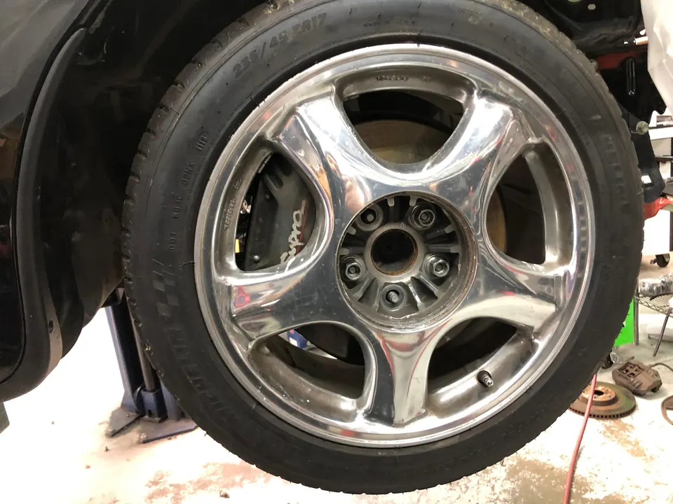 Close-up of a Toyota Supra wheel and brake caliper on a lift in a shop.