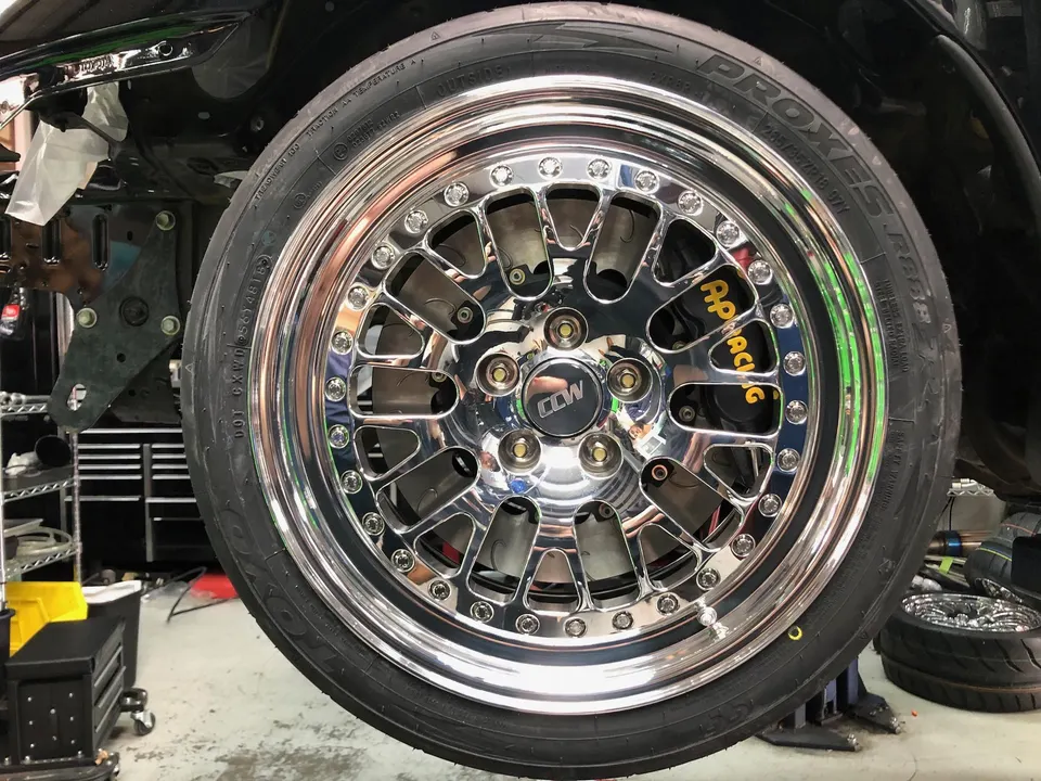 A close-up of a chrome CCW wheel with AP Racing brakes and Toyo Proxes tires in a shop setting.
