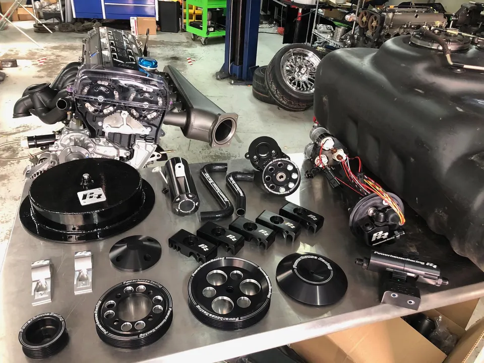 High-performance 2JZ engine with clear cam cover and fuel system components on a shop table.