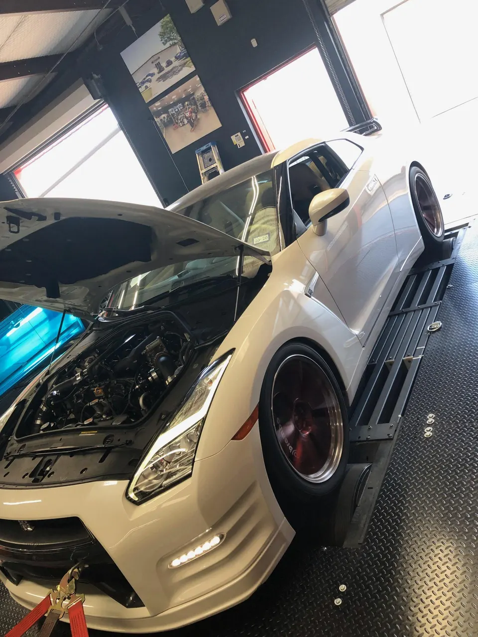 A white Nissan GT-R strapped to a dyno with its hood open, showcasing the engine bay and aftermarket wheels.