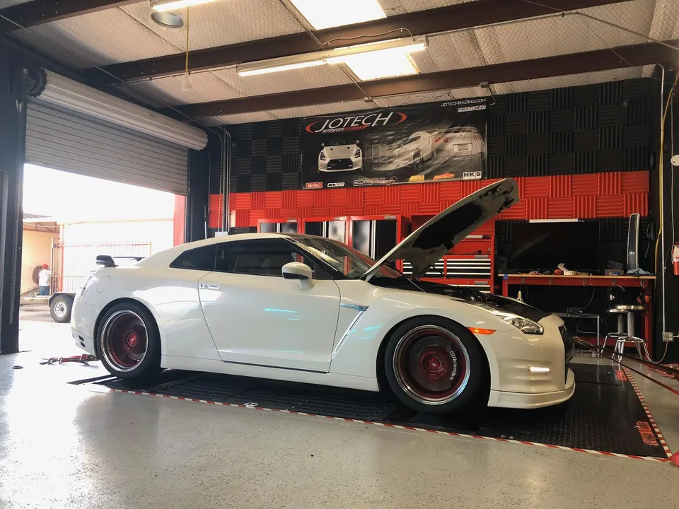 White Nissan GT-R with its hood open, parked on a dyno at a performance tuning shop.