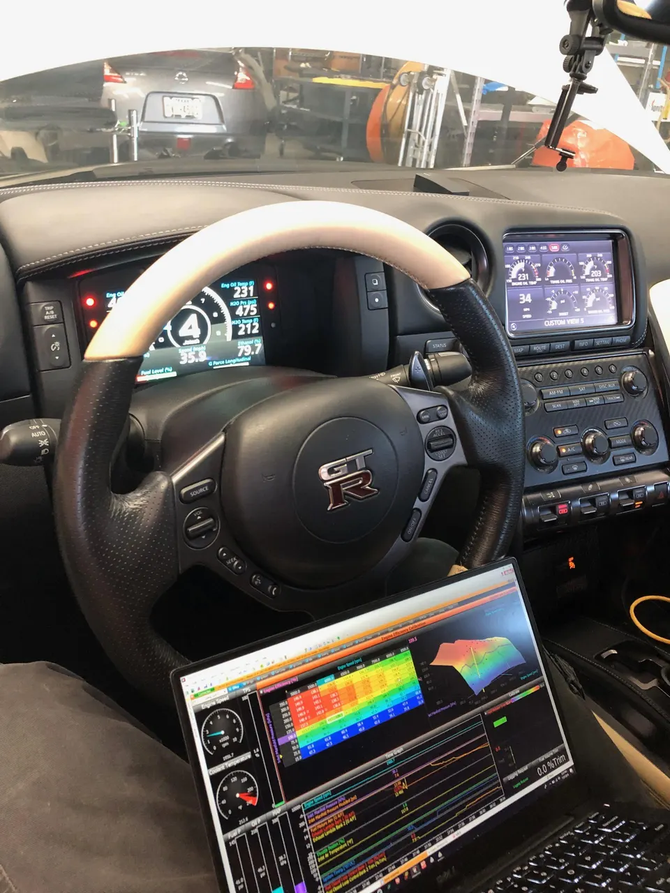 Nissan GT-R interior with a laptop displaying engine tuning software, indicating work in a shop environment.
