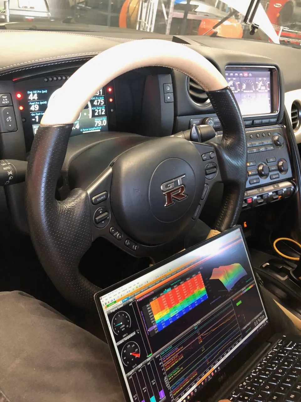 Interior view of a Nissan GT-R with a laptop displaying tuning software and dashboard gauges showing engine parameters.