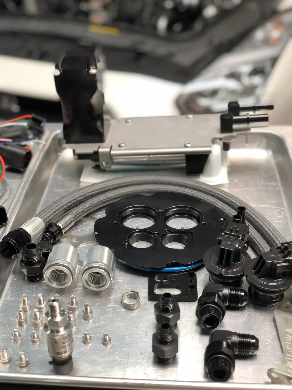 Performance fuel system components including fuel lines, injectors, and fittings laid out on a tray in a shop.