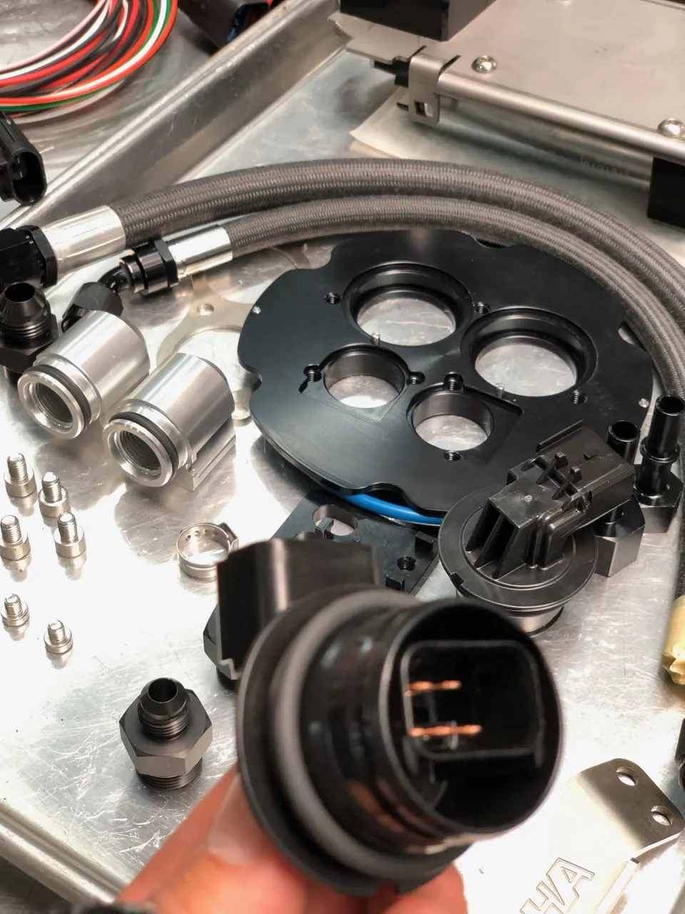 Various performance fuel system components including braided lines, AN fittings, and fuel pump parts laid out on a workbench.