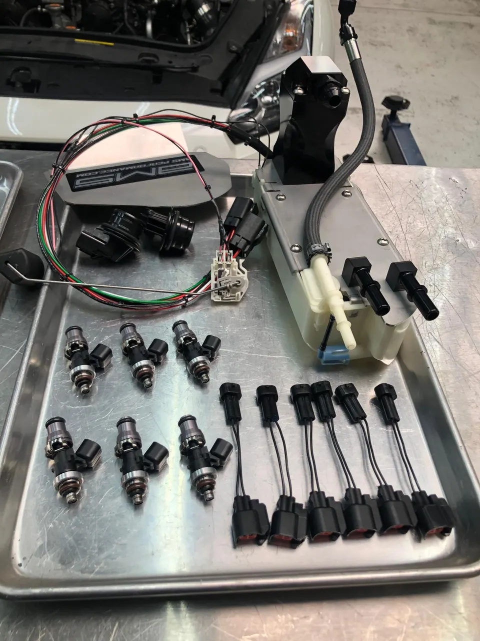 Aftermarket fuel system components including injectors, fuel pump, and wiring harnesses laid out on a tray in a performance shop.