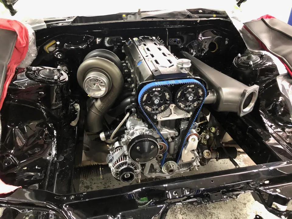 High-performance engine bay with a large turbocharger, custom intake manifold, and blue timing belt during a build at a performance shop.