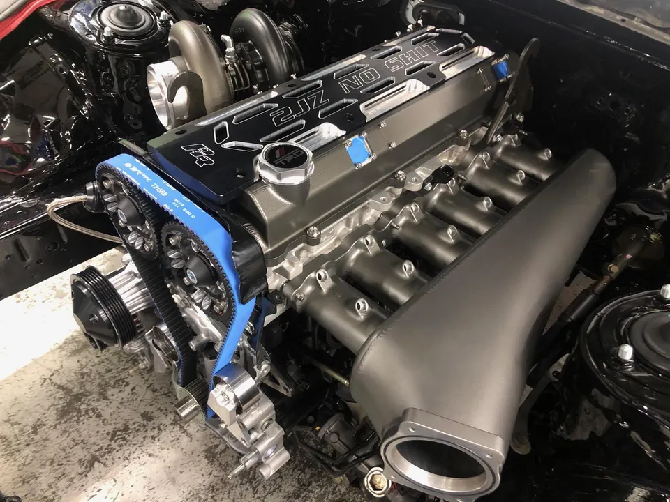Highly modified 2JZ engine with custom intake manifold, turbocharger, and blue timing belt in a clean engine bay.