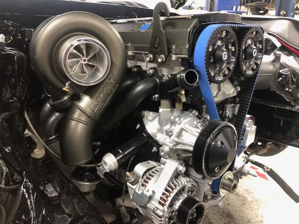 A close-up of a high-performance engine bay featuring a large Precision turbocharger and blue timing belt.