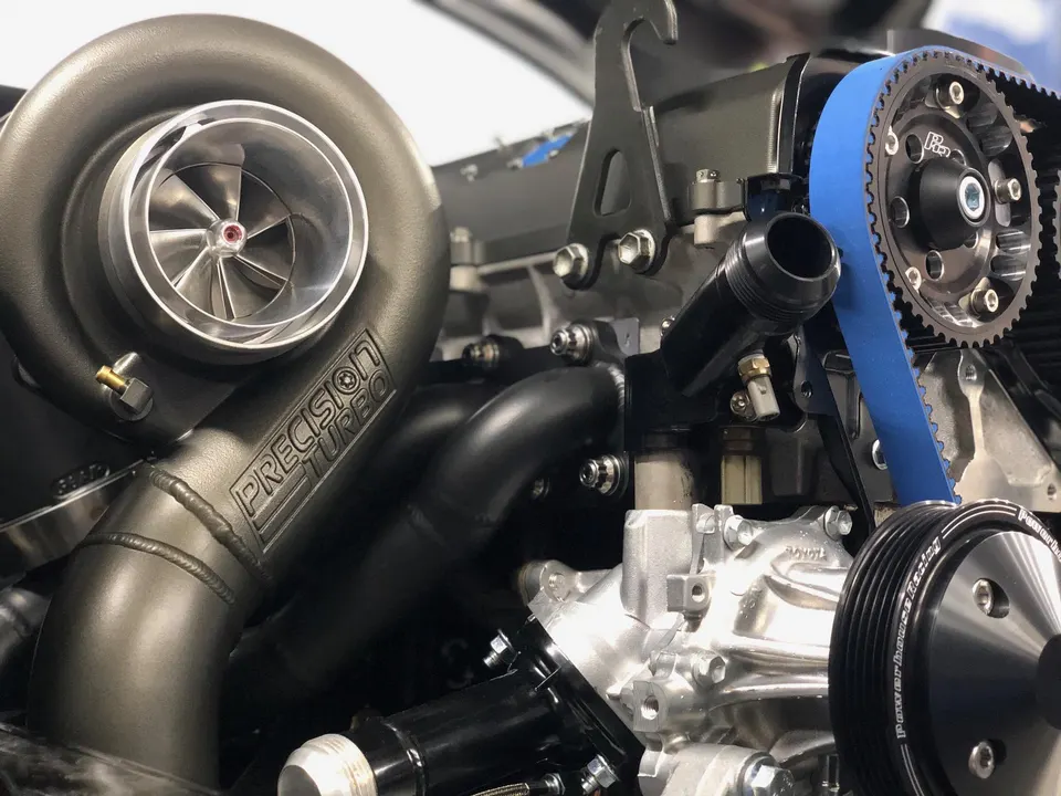 A close-up of a Precision Turbo turbocharger and a blue timing belt on a performance engine.