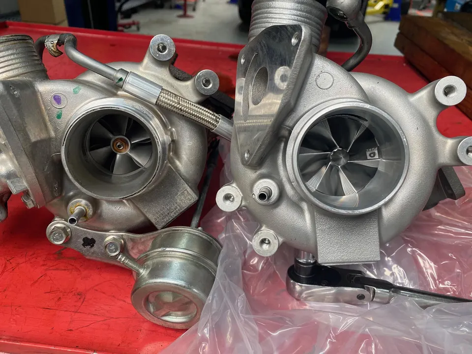Two performance turbochargers, one with a Pure Turbos compressor wheel, on a red workbench in a shop setting.